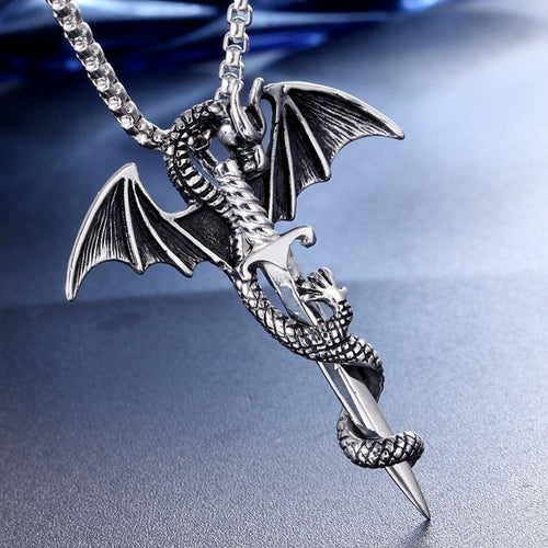 The Flying Dragon With Sword Necklace by Yellow Pandora is a silver alloy pendant showcasing an intricately detailed dragon with wings extended, gripping a sword as its body coils around the blade. The dark blue and silver gradient background enhances the metallic luster of this striking piece.