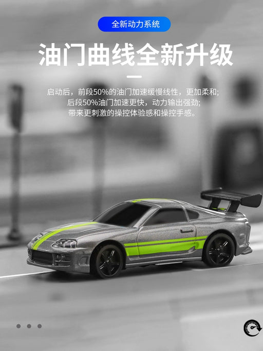 A close-up image of a Turbo1/76 Miniature RC Remote Control Electric Sports Car from Lacatang Shop on a racing track, featuring a sleek silver body with green racing stripes. This realistic Toyota mini desktop remote control car boasts a prominent rear spoiler and is positioned slightly to the right. The background is blurred, with Chinese text overlayed at the top and sides.