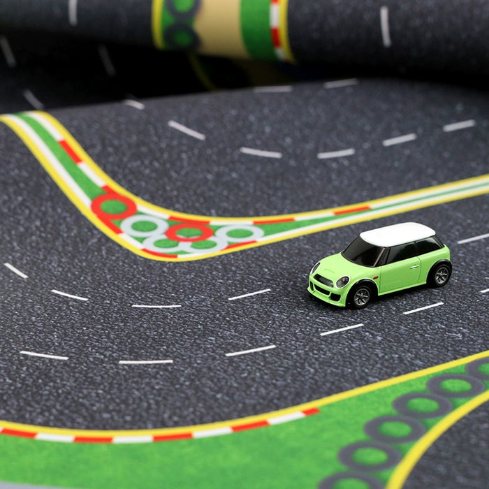 A small green toy car with a white roof races down the Turbo Mini Drift Scene Remote Control Car Track by Lacatang Shop, featuring curves, lane markings, and decorative elements like tire tracks and curbs for a thrilling drifting experience.