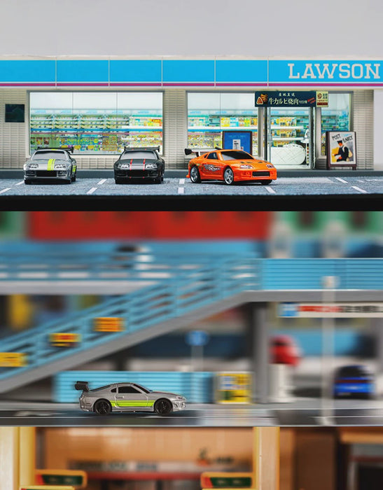 A row of toy cars, featuring various models in black, red, and gray, are parked in front of a miniature Lawson convenience store. In the blurred background, a Turbo1/76 Miniature RC Remote Control Electric Sports Car by Lacatang Shop zooms over an elevated roadway, adding excitement to the scene.