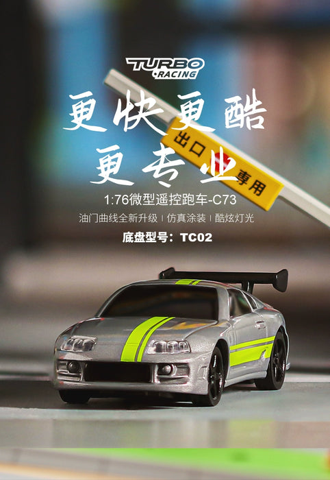 A miniature silver electric sports car with bright green racing stripes and yellow details is displayed on a dark surface. Above the car are Chinese characters and the text "TURBO RACING" along with a model identifier "TC02". A yellow road sign is visible in the background. This toy is part of the Lacatang Shop's collection, specifically the Turbo1/76 Miniature RC Remote Control Electric Sports Car C71 C72 C73 Simulation Toyota Mini Desktop Remote Control Car.