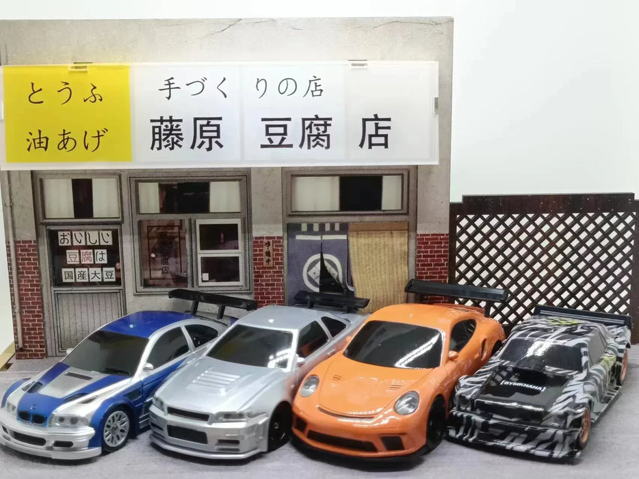 Four models from Lacatang Shop, which include a silver sports car, a white sedan with a spoiler, an orange Porsche, and a black race car, are parked in front of a miniature building that features a sign with Japanese text. Each 2.4G RC Drift Car 1/43 by Lacatang Shop promises high speed and four-wheel drive capabilities for thrilling races.