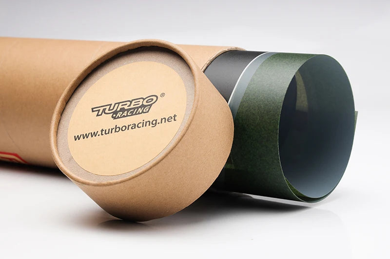 A cardboard tube labeled "TURBO RACING 1:76" reveals a poster showcasing its drift and jump features. The lid, featuring "www.turboracing.net," sits nearby, appealing to Lacatang Shop's remote control car track set enthusiasts.