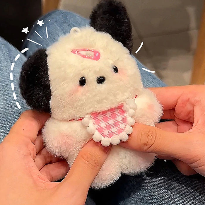 A person holds a Cute Plush Puppy Keychain by Lacatang Shop featuring black ears and a pink checkered bib with a small pink hat. Set against blue jeans and surrounded by white doodles, it's an adorable cartoon bag charm or perfect birthday gift for women and girls.