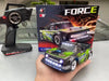 A hand holds the WLtoys 1:28 284131 284161, a black and green remote-controlled truck from Lacatang Shop with its headlights on. Behind it, the original box showcases an image of the truck alongside the prominently displayed word "FORCE." Next to the box is the remote control unit, which includes a powerful lithium battery.