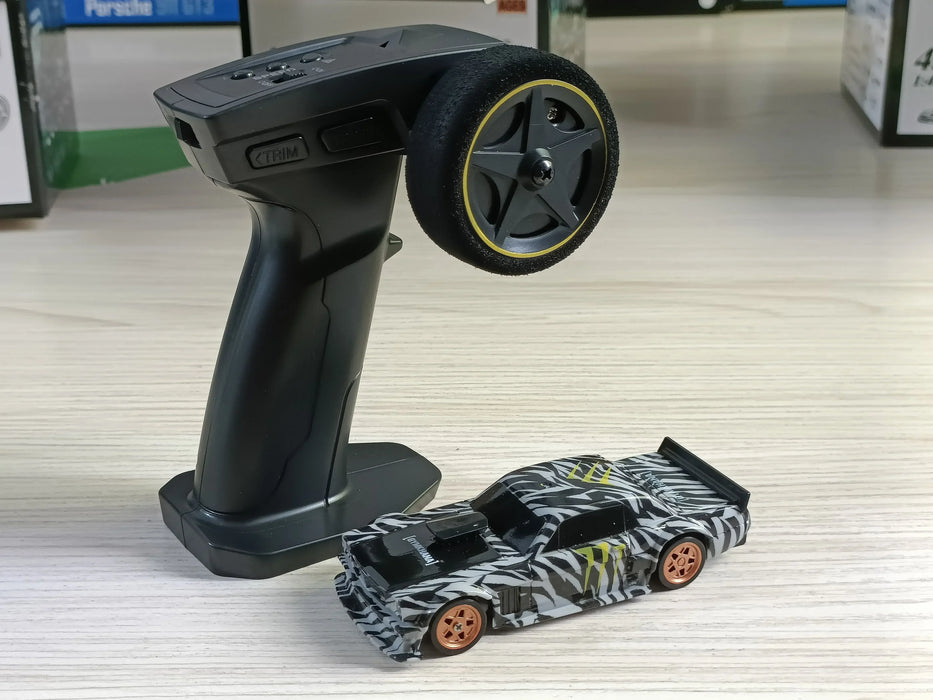 A black and gray remote control with a large dial stands next to the Lacatang Shop's 2.4G RC Drift Car 1/43 4WD Remote Control Car: a sleek, high-speed racing toy adorned with a zebra-striped design, orange wheels, and black details, all set on a light wood surface.