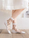 Someone wearing Lacatang Shop's Vintage Floral Lace Ruffle Socks, featuring embroidered pink flowers and green leaves, stands on a wooden floor. Paired with a white knee-length skirt, the scene exudes a light and airy feel reminiscent of transparent crystal silk elegance.