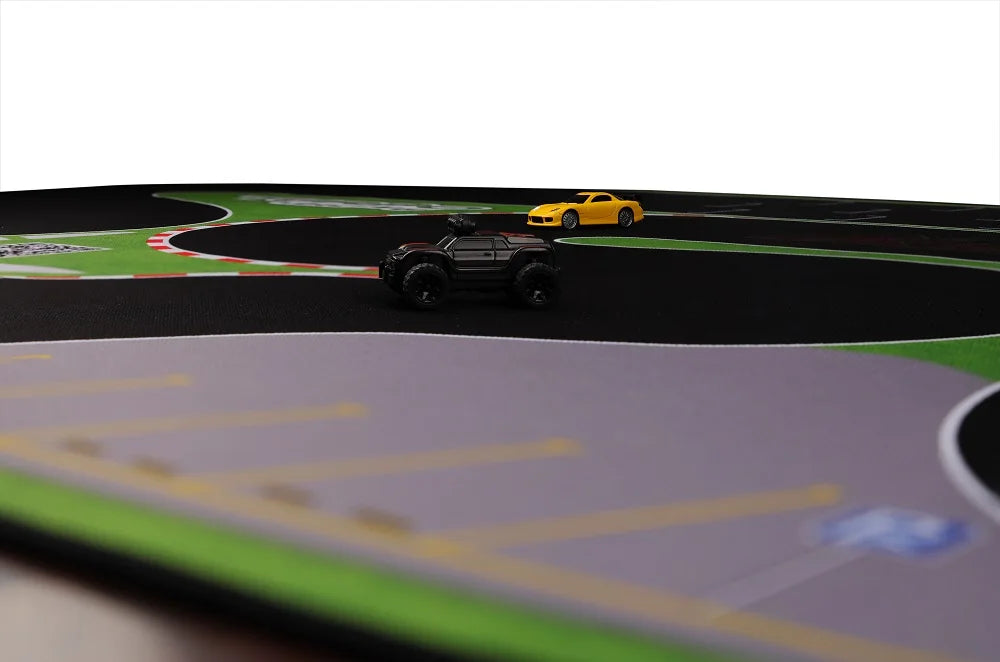 On the vibrant Lacatang Shop's Portable Turbo Racing Rubber Track Mat 1600x900mm, a black 1:76 RC mini car is featured on a gray section, while a yellow car races further back amid green areas and red-and-white curbs—an ideal accessory for racing enthusiasts of table fun.