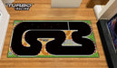 A Lacatang Shop Portable Turbo Racing Rubber Mat for 1:76 RC Mini Car Track, featuring white and red borders, a checkered finish line, and the "Turbo Racing" logo, lies on a wooden floor with its circuit design.