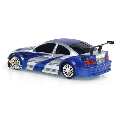 A toy car modeled to resemble a sporty blue and silver race car with a large rear spoiler and intricate detailing, including blue racing stripes. The logo of "Lacatang Shop" is visible near the back wheel. This 1/43 scale drift car, called the Gifts Outdoor Toys 1/43 RC Mini Race Cars 2.4g Radio Control Drift Car 4WD High-Speed Motor Vehicle Model for Boys TH23884, is positioned on a reflective white surface.