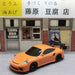 A 2.4G RC Drift Car 1/43 4WD Remote Control Car, branded by Lacatang Shop, featuring a high-speed design with an orange body and black rear spoiler, is parked in front of a small storefront. Signs above the store are in Japanese, displaying large black kanji (藤原豆腐店) that translate to "Fujiwara Tofu Shop." The background highlights traditional sliding doors and windows.