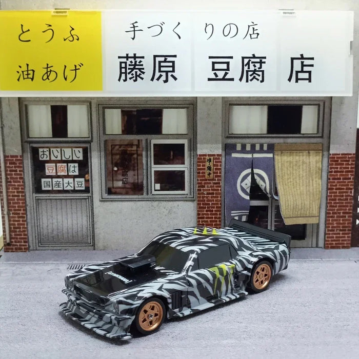 A model of the Lacatang Shop 2.4G RC Drift Car 1/43 with an abstract black and white paint design and gold wheels is parked in front of a building. The building features Japanese signage, indicating it is a tofu shop. The shop has a traditional exterior with brick walls and large windows.