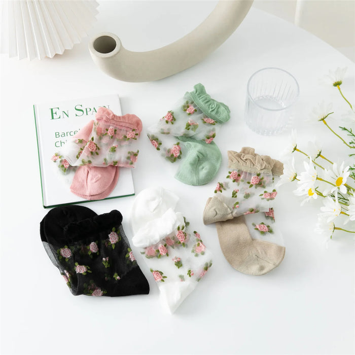 Lacatang Shop's Vintage Floral Lace Ruffle Socks for Women, in vibrant Kawaii Harajuku style, are displayed on a white surface with a partially visible book, clear glass, curved vase, and white flowers enhancing the aesthetic.