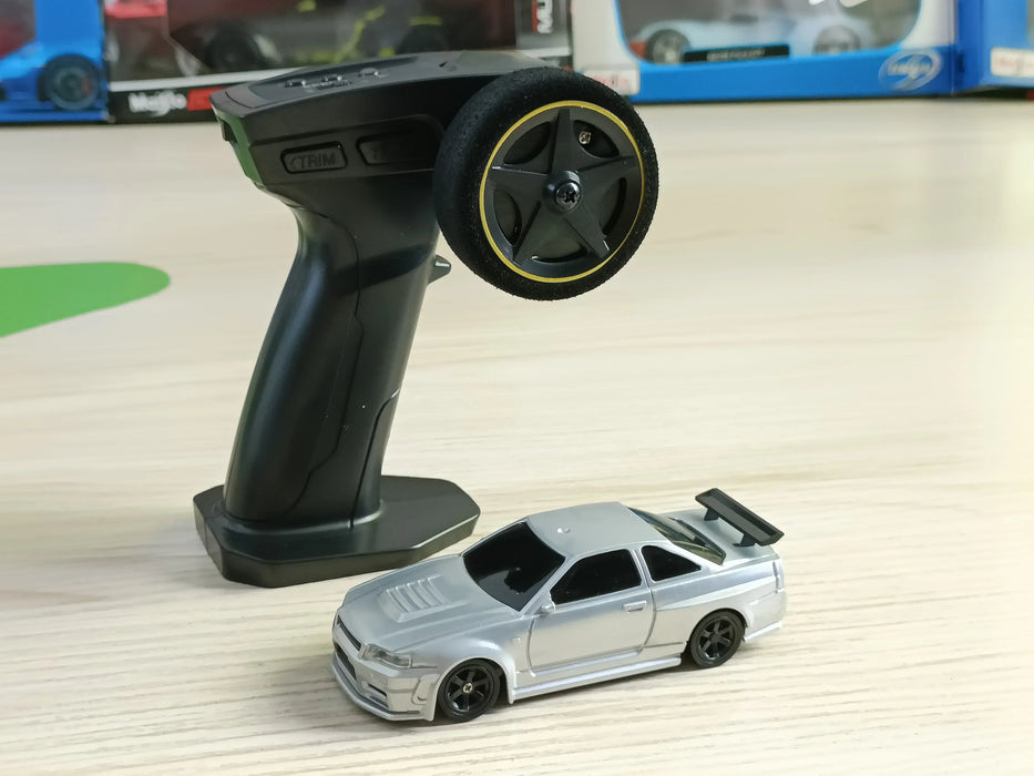 A black remote control and a small silver Lacatang Shop 2.4G RC Drift Car are placed on a wooden surface. The high-speed racing car, designed for four-wheel drive performance, features a spoiler and black wheels. Blurred in the background are boxes containing other toy cars.