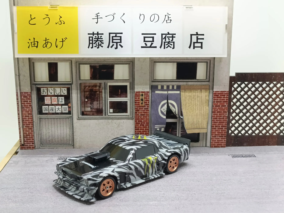 A Lacatang Shop 2.4G RC Drift Car 1/43 scale, featuring a high-speed four-wheel drive and a zebra stripe pattern with striking orange wheels, is parked in front of a detailed model of a traditional Japanese tofu shop. The shop boasts white and yellow signage above wooden latticework and sliding doors.