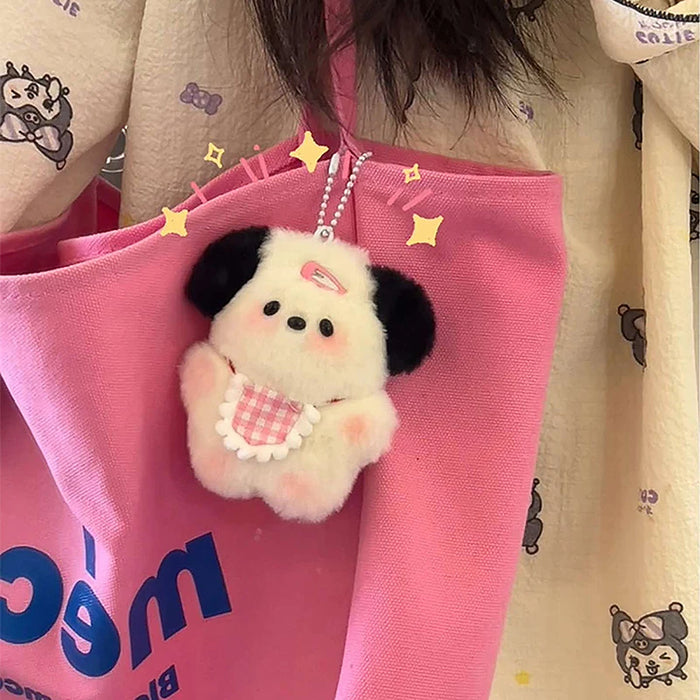 A Cute Plush Puppy Keychain from Lacatang Shop, the adorable cartoon bag charm, complements a pink bag. With black ears and a checkered pink bow, it sparkles as it hangs beside a person wearing a cream shirt with cartoon patterns—a perfect birthday gift for women and girls!.