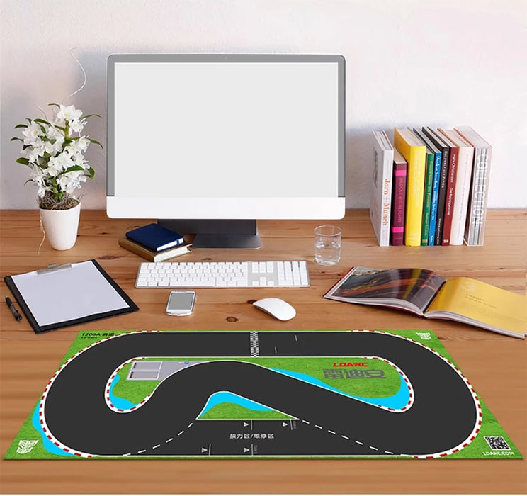 A desk with a computer, keyboard, and mouse is accompanied by a small plant, glass of water, and stack of books. A Lacatang Shop's LDARC V64 Mini RC Car Racing Track Mat adds a playful vibe to this customizable setup.