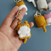 A hand holding a Cute Cat Crochet Keychain from Lacatang Shop, featuring a small, yellow, cat-like character with white feet and belly. Several similar Cute Cat Crochet Keychains in different colors are visible in the background. These keychains, known as Cute Cat Crochet Keychains Knitting Cartoon Cat Doll Keyrings For Car Keys Kawaii Small Cat Knitted Keychain For Bag Pendant New, feature sturdy zinc alloy rings and are perfect for adding charm to your accessories.