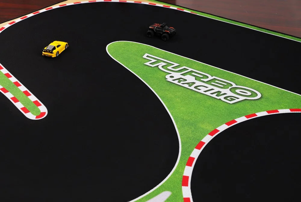 The Lacatang Shop's Portable Turbo Racing Rubber Track Mat 1600x900mm is a fun table racing accessory for two 1:76 RC mini cars—a yellow sports car and a black truck. It features a green area with "Turbo Racing" printed on it, along with red and white striped borders.