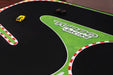 Close-up of Lacatang Shop's Portable Turbo Racing Track Mat (1600x900mm) featuring a yellow and a black mini car. The track showcases red and white stripes, with "Turbo Racing" on its green section for an enhanced racing experience. Suitable for 1/76, 1/64, 1/58 scale mini cars.