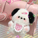 The Lacatang Shop Adorable Plush Puppy Keychain is a cute cartoon bag charm with black ears, a pink checkered bib, and a small pink hair clip. Perfect for pink bags, it features colorful heart effects and makes an ideal gift for those who love adorable accessories.