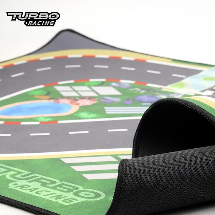 A close-up of the Lacatang Shop Portable Turbo Racing Rubber Mat reveals roads, a pool, and lush greenery. One corner is rolled up to show thickness. The "Turbo Racing" logo is visible, ideal for 1:76 RC Mini Car Track adventures and available in various sizes for table racing enthusiasts.