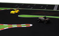 Lacatang Shop's Portable Turbo Racing Track Mat (1600x900mm) lets mini scale cars speed along green and red markings. The yellow car outpaces the black one near a curve, creating an exciting miniature race experience.