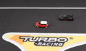 Two miniature cars speed on a Lacatang Shop's Portable Turbo Racing Rubber Mat for 1:76 RC Mini Car Track. The red and white car leads the black one, with the "Turbo Racing" logo clearly displayed.