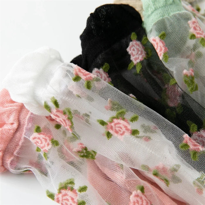 The Lacatang Shop's Vintage Floral Lace Ruffle Socks for women showcase sheer, transparent crystal silk adorned with pink roses and green leaves. These ultra-thin crew socks layer white, black, and pink hues, embodying Kawaii Harajuku style.