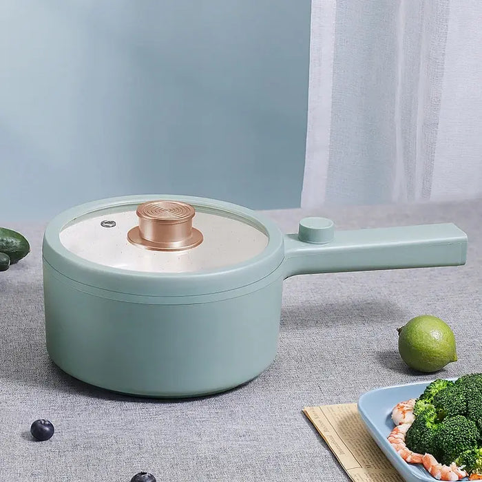 A pastel green 2024 New Portable 1.5L Multi-function Pot Rice Cooker Electric Cooking Stir Frying Noodle Pot Mini Hot Pot Household Dormitory from Lacatang Shop with a lid sits on a grey countertop. The lid features a golden knob, and the hot pot has an elongated handle. Next to it is a blue plate containing a meal of broccoli and shrimp, accompanied by a lime.