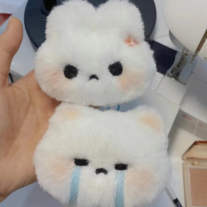 A person holds two high-quality, fluffy white plush rabbit-shaped accessories from Lacatang Shop, which are part of the "Cartoon Plush Rabbit Doll Toy Keychain Sweet Cute Bag Pendant Charms Car Keyring Accessories For Women Couples Kawaii Gift" collection. The top rabbit has black eyes and a neutral expression, while the bottom rabbit has blue tears under its eyes, indicating it's sad. Both are made of soft, plush material.