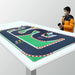 A person in an orange jacket stands by a table with the Lacatang Shop Portable Mini RC Car Race Track Mat (PK mesh cloth, 160x90cm & 120x60cm) featuring black with red and white barriers. They appear to be holding a remote control for the 1/76 scale RC cars in various colors.