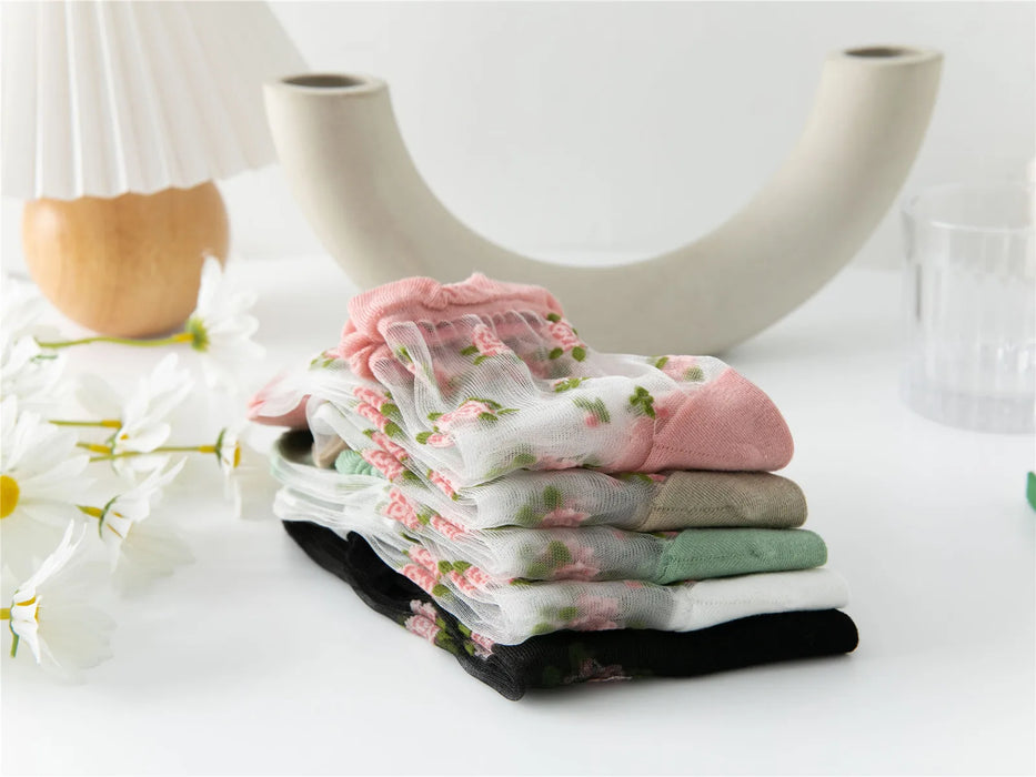 A set of Lacatang Shop's Vintage Floral Lace Ruffle Socks, designed in kawaii Harajuku style and available in colors like pink, white, and green, is neatly displayed on a white surface with decor elements such as a ceramic vase, daisies, and a modern lamp enhancing their aesthetic appeal.