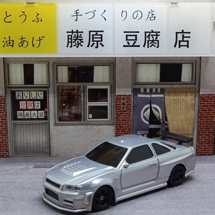 A 2.4G RC Drift Car by Lacatang Shop, featuring a sleek silver 4WD design, is parked outside a small beige shop with large windows and a sign in Japanese that reads "Handmade Tofu Shop." The store's window displays a small menu. The mini racing car model boasts a black spoiler and tinted windows.