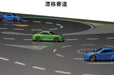 The Lacatang Shop's TURBO RACING 1:76 Remote Control Car Race Track Set includes drifts, jumps, and cement obstacles. It showcases a winding road with green and blue racer cars, white dashed lane markings, directional arrows, and blue speedsters in the background ready for action.