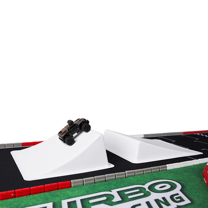 A Lacatang Shop TURBO RACING 1:76 RC car races on a track with jump and drift features, surrounded by red and gray barriers. The foreground displays "TURBO RACING.