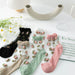 A white table displays Lacatang Shop's Vintage Floral Lace Ruffle Socks for Women in Kawaii Harajuku style, featuring transparent crystal silk in black, white, beige, green, and pink. A curved vase holds daisies beside a book titled "En Spain.