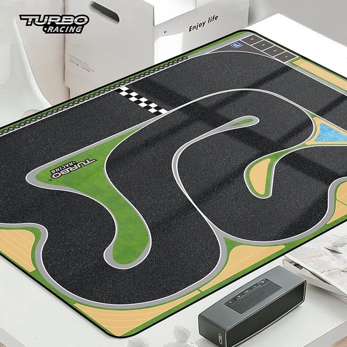 The Lacatang Shop's TURBO RACING 1:76 Remote Control Car Track Set features a rectangular mat with winding asphalt paths, green grass areas, and a checkered start/finish line. It's ideal for showcasing your car's jump and drift capabilities, presented beside a black box on a white surface.