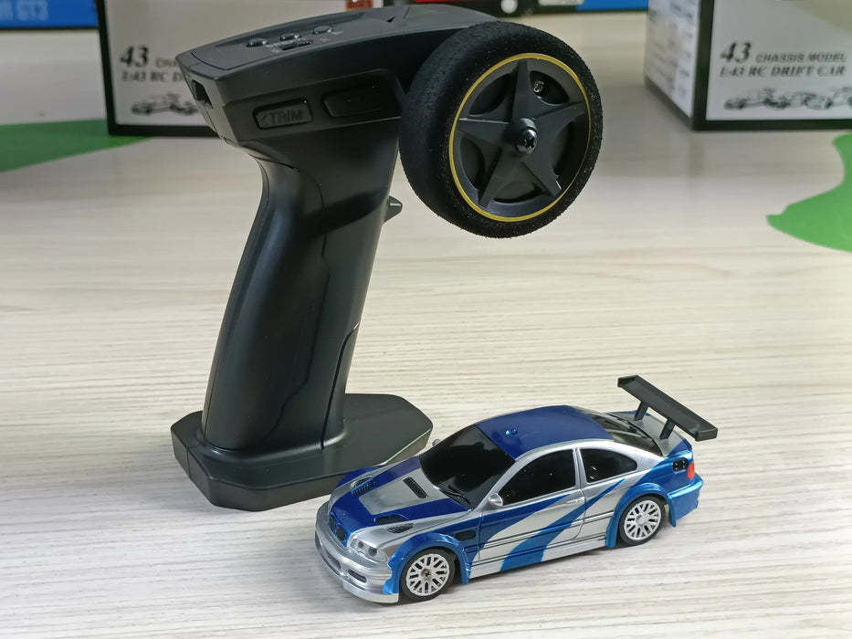 A Lacatang Shop 2.4G RC Drift Car 1/43 4WD Remote Control Car High Speed Four Wheel Drive Radio Controlled Mini Racing Car, featuring a black remote control with a steering wheel and buttons, alongside a small blue racing car with silver detailing, racing stripes, and a spoiler on a light-colored surface.