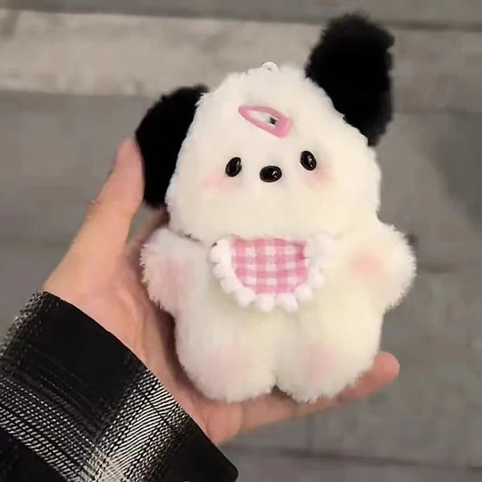 A plush puppy keychain with pink cheeks and a checkered bib from Lacatang Shop rests in a plaid shirt-wearing hand. This charming piece is a perfect birthday gift for women and girls, ideal as a cartoon bag charm against a neutral, blurred background.