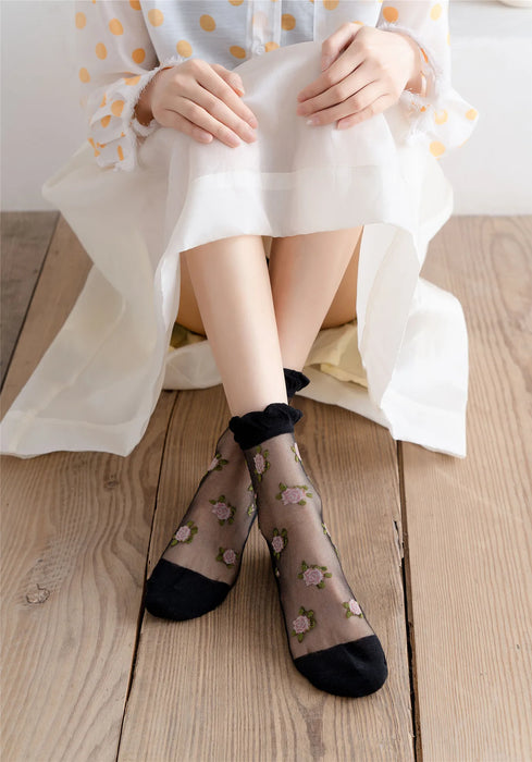 A person sits on a wooden floor wearing Lacatang Shop's Vintage Floral Lace Ruffle Socks, paired with a light, semi-transparent white polka dot skirt. Their hands rest on the skirt's hem and legs are bent at the knees, capturing a hint of Kawaii Harajuku style.