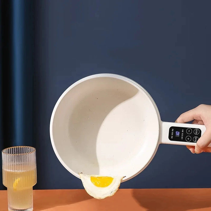 A person tilts a white 1.6L Lacatang Shop Smart Electric Cooking Pot Reservation Multifunctional Non-stick Electric Wok Household Electric Hot Pot With Steamer 220V, using its electronic handle display, causing a cooked egg to slide out onto an orange countertop. Nearby, a glass of water with a lemon slice sits against a dark blue background.