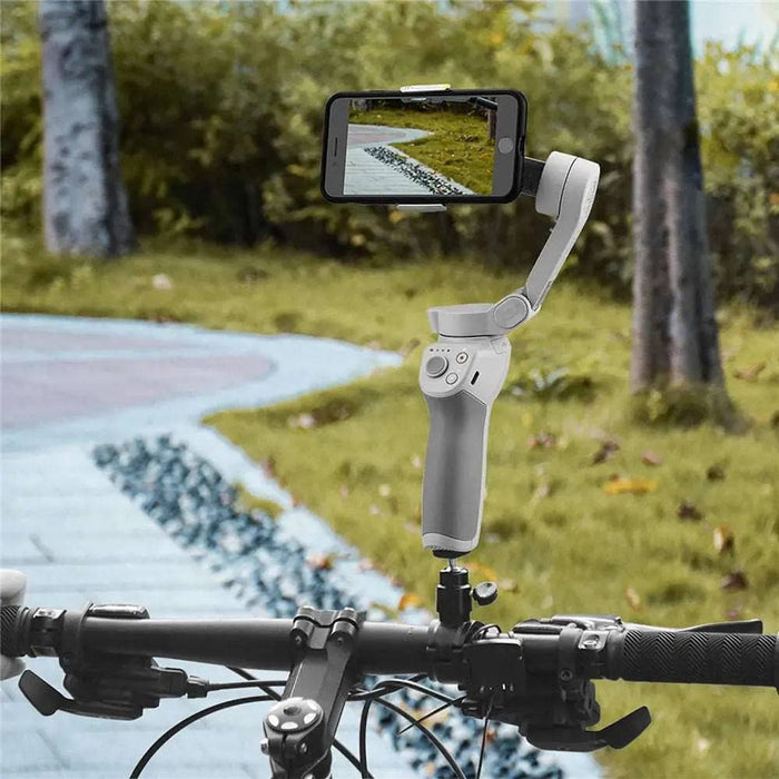 A sleek, stainless steel nose hair trimmer from AliExpress is mounted on the handlebars of a bicycle. The smartphone’s screen displays a video of a winding path through a grassy area with trees in the background. The bicycle is on the same path, suggesting it is capturing the scenery ahead.